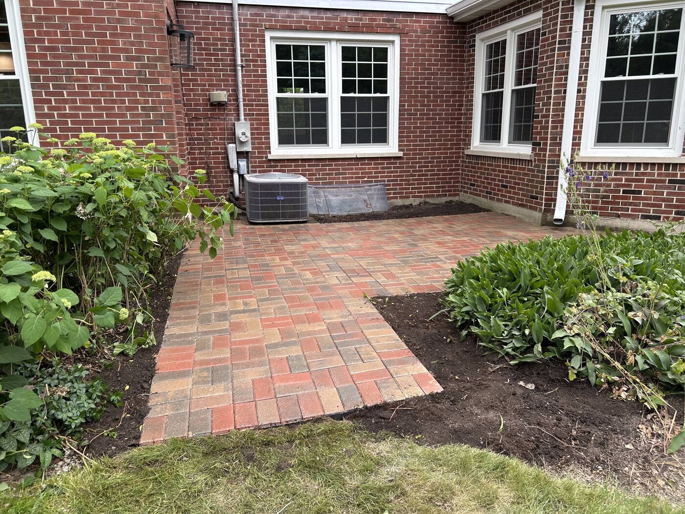 New brick paver patio with clean, level joints installed against the rear of a brick home