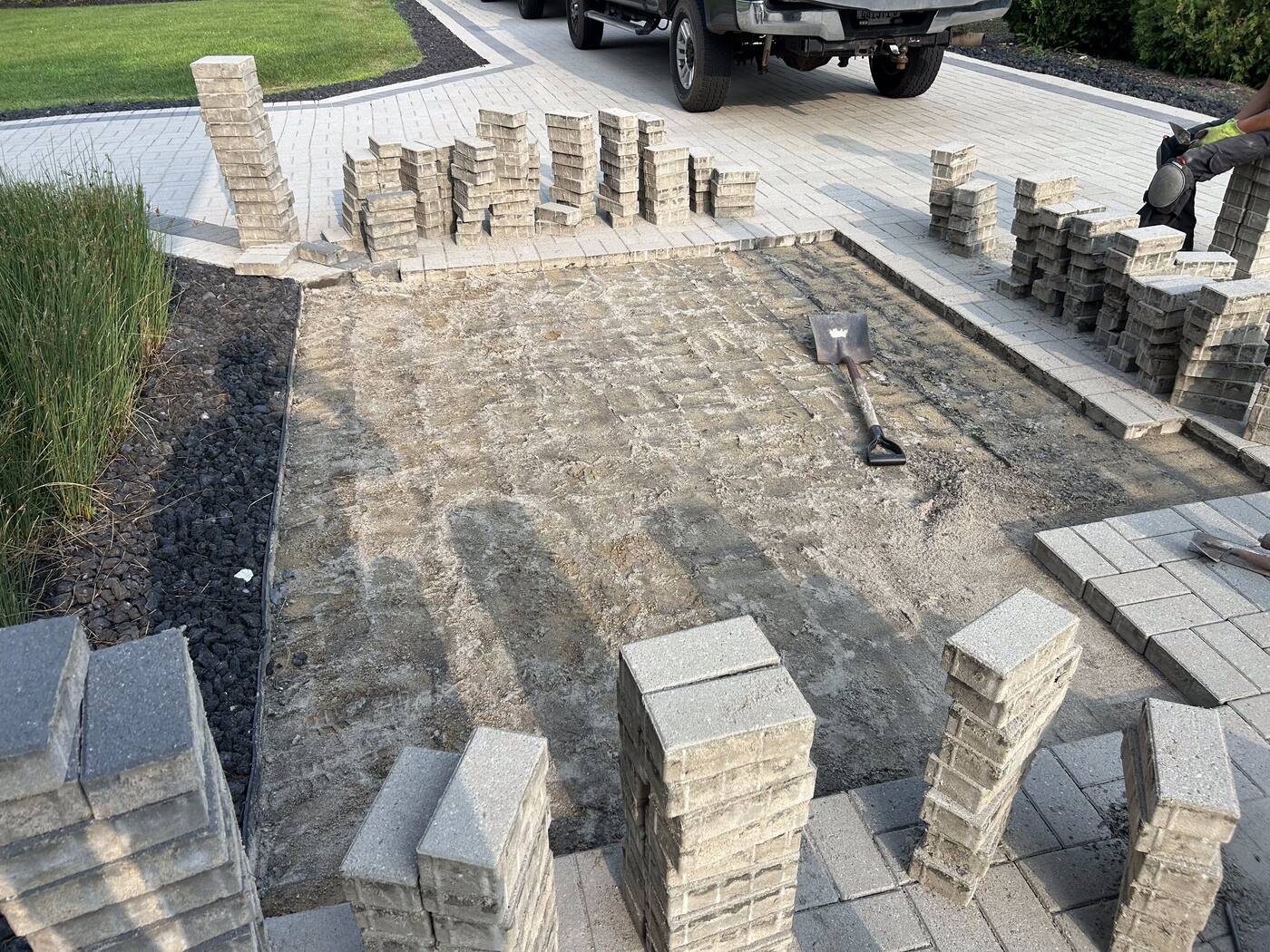 Prepared gravel base with stacked paver bundles ready for a new patio installation