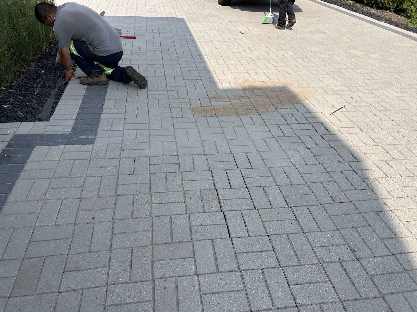 Crew installing gray paver stones with a dark contrasting border during patio construction