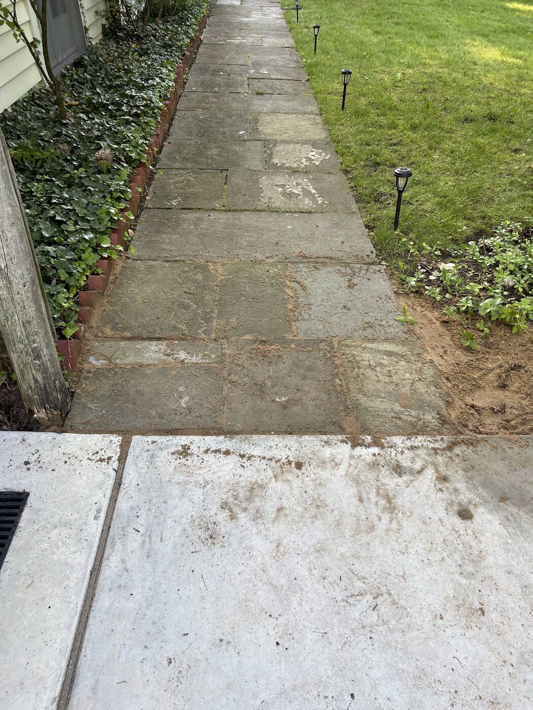 Settled, uneven stone walkway pavers along the side of a home