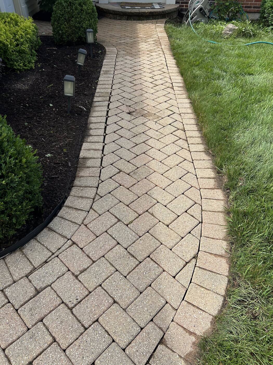 Herringbone-pattern brick walkway with landscape lighting leading to a front entry